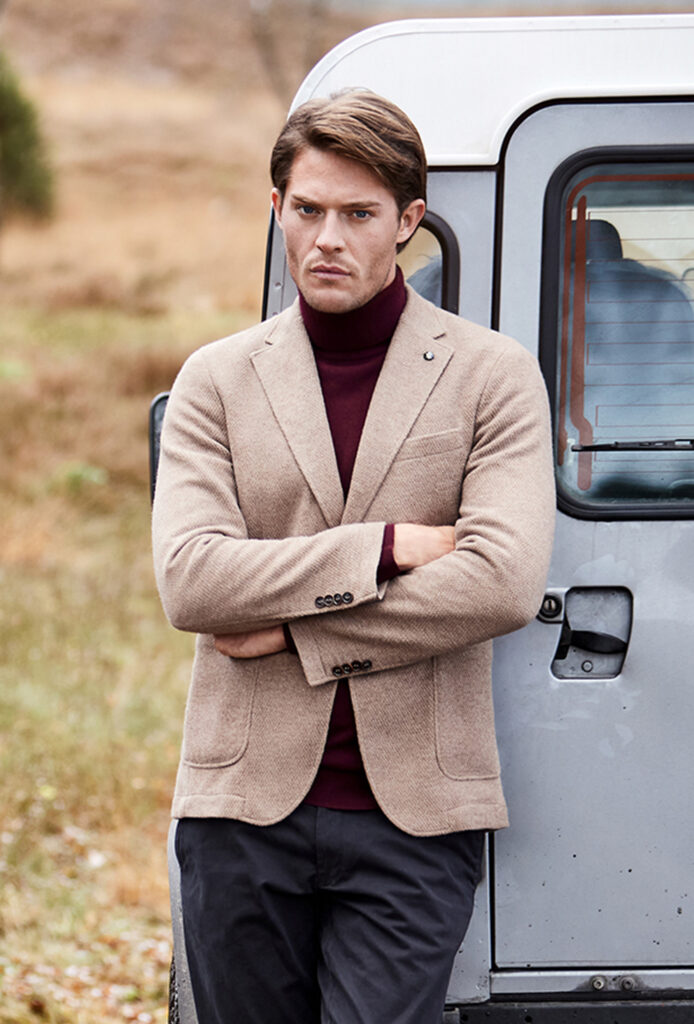 Young man with brown hair in beige jacket, wine-red turtleneck jumper and dark trousers